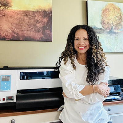 Woman standing in front of a large printer with artwork on the wall behind her