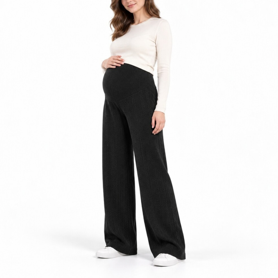 A pregnant woman modeling black wide-leg ribbed maternity pants with a matching high-waisted top, standing against a solid white studio background.