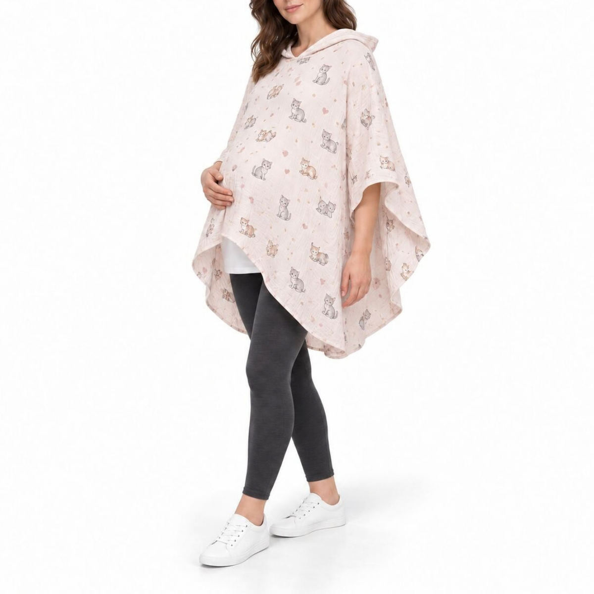 A woman modeling a light pink maternity poncho with a white cat pattern, paired with dark gray leggings and white sneakers, against a plain white background.