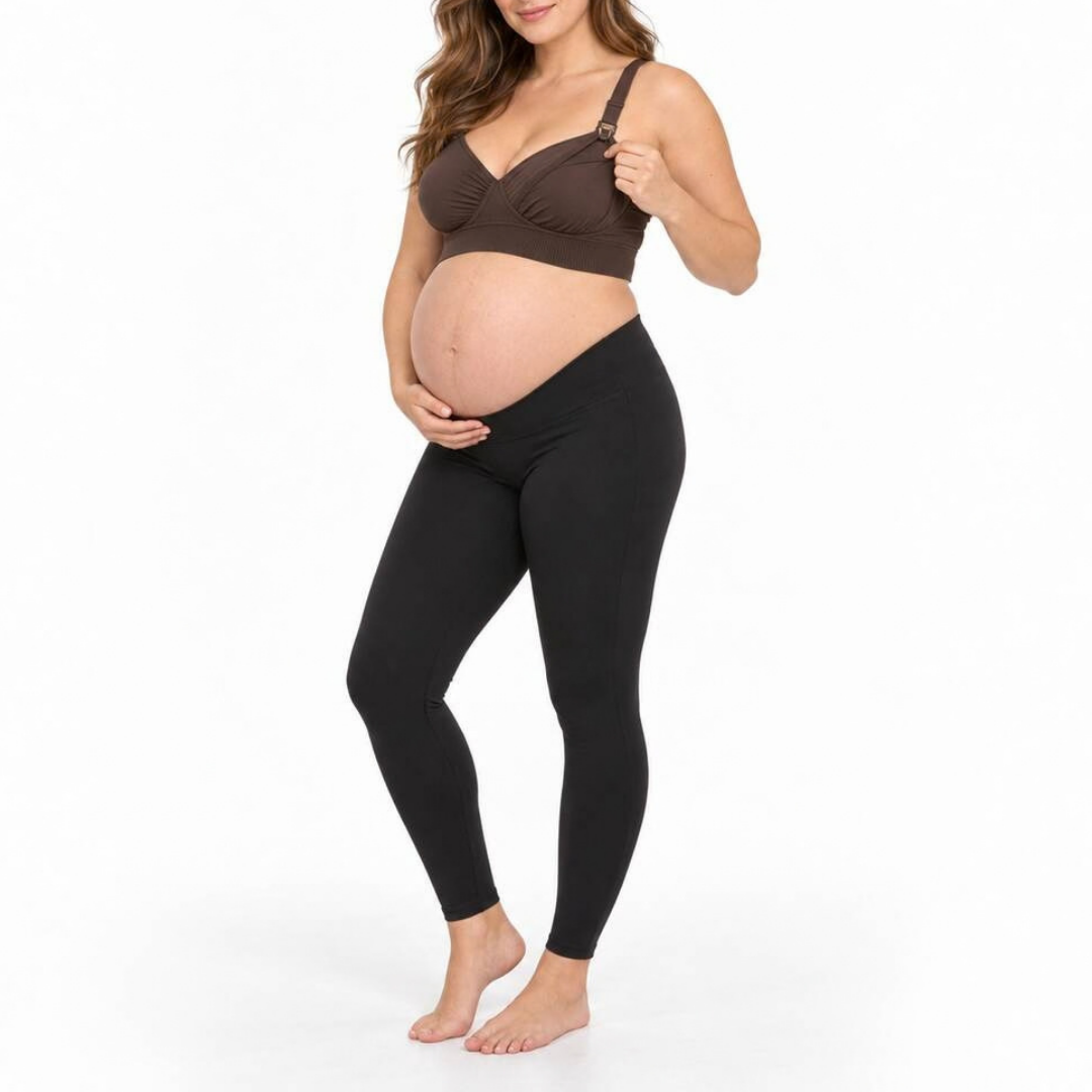 A pregnant model wearing a brown maternity bra and black leggings, standing against a plain white studio background.