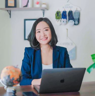 Woman sitting at a desk with a laptop, smiling in an office setting.